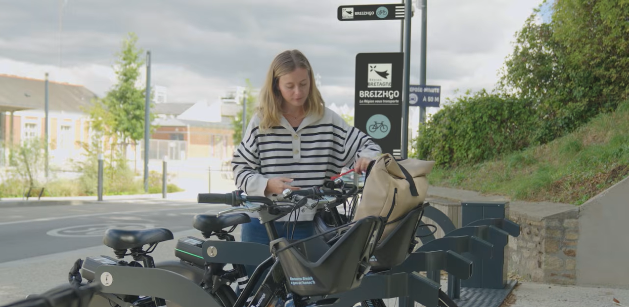 Une voyageuse loue un vélo électrique en libre-service dans une gare du réseau BreizhGo.